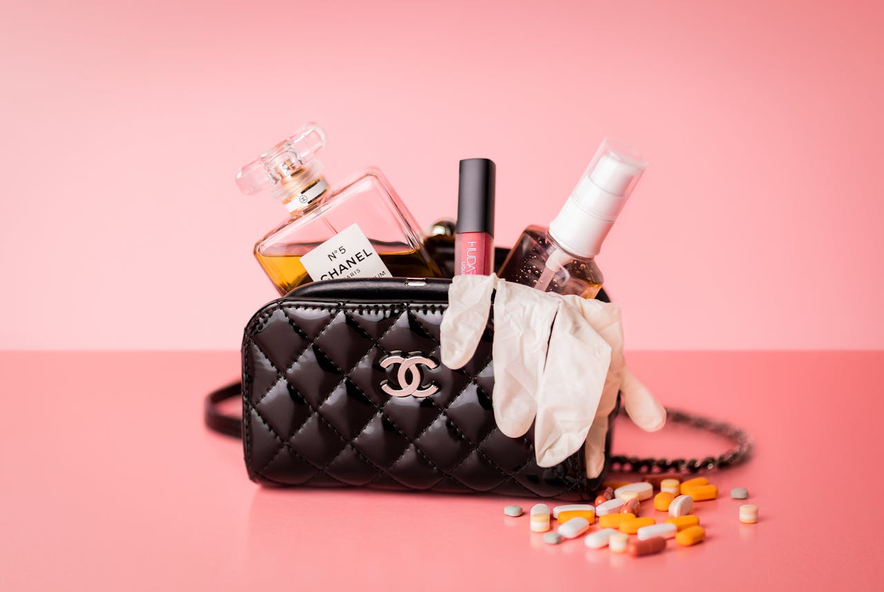 Chanel bag featuring perfume, gloves, and medicines on a pink surface for a mix of luxury and health.